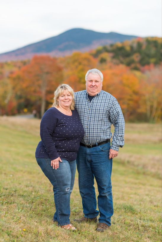 Couple standing on a grassy field with autumn trees and a mountain in the background