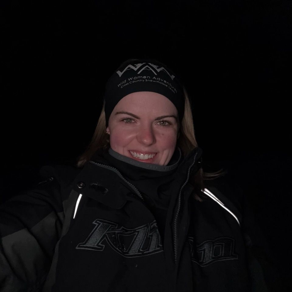 Smiling person in black winter clothing and beanie against a dark background