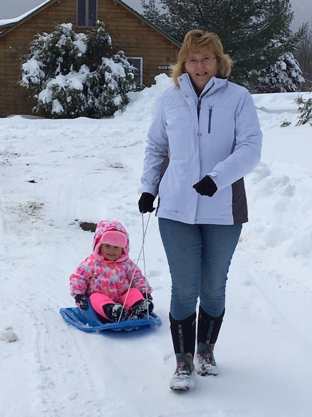 Woman standing in snow while child rides a blue sled behind her