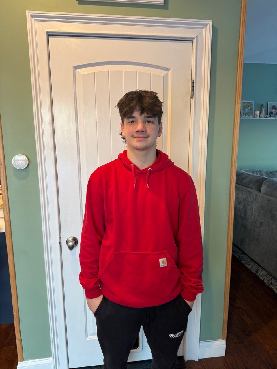 Person in a red hoodie and black pants standing indoors in front of a white door.