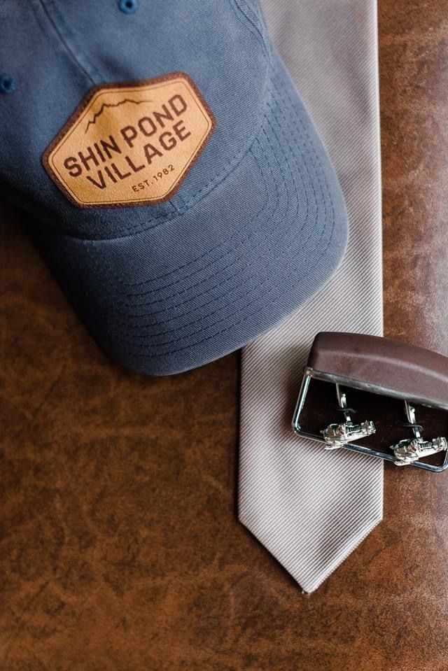 Blue cap, gray tie, and silver belt buckle on a brown leather surface.
