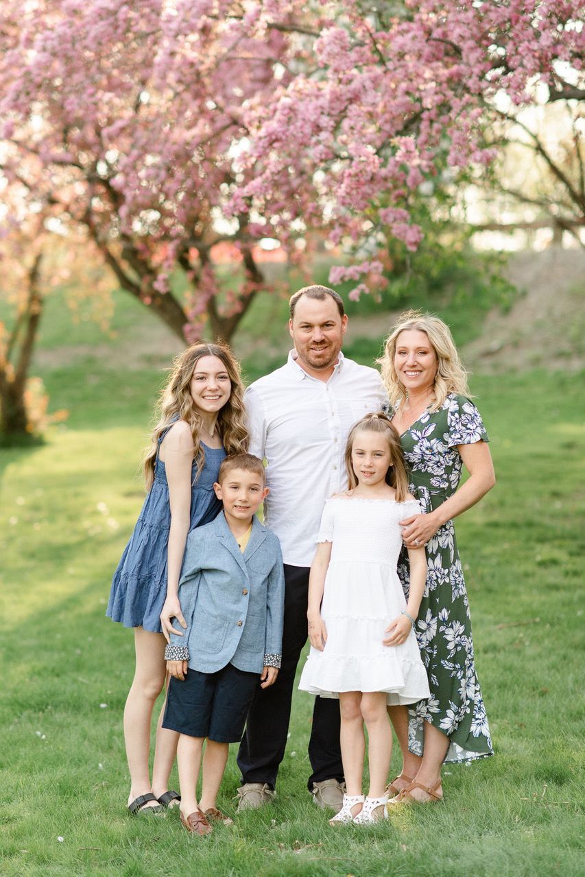 Family standing together in a grassy park beneath pink flowering trees