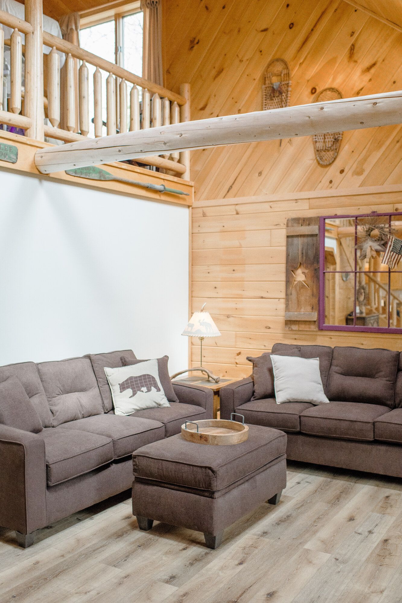 Cozy wood-paneled loft living room with two gray sofas, coffee table, and soft lighting.