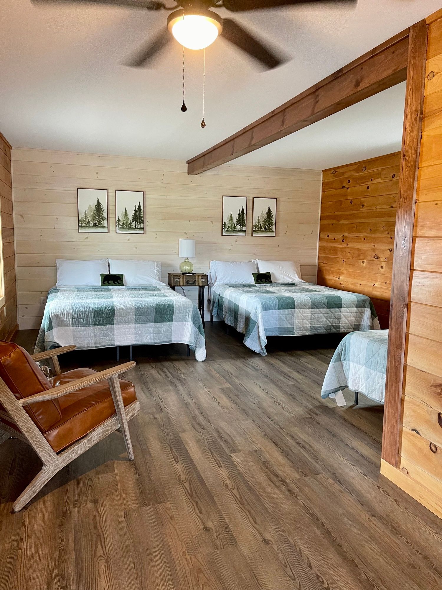 Cozy cabin bedroom with two twin beds, wooden walls, a chair, and ceiling fan
