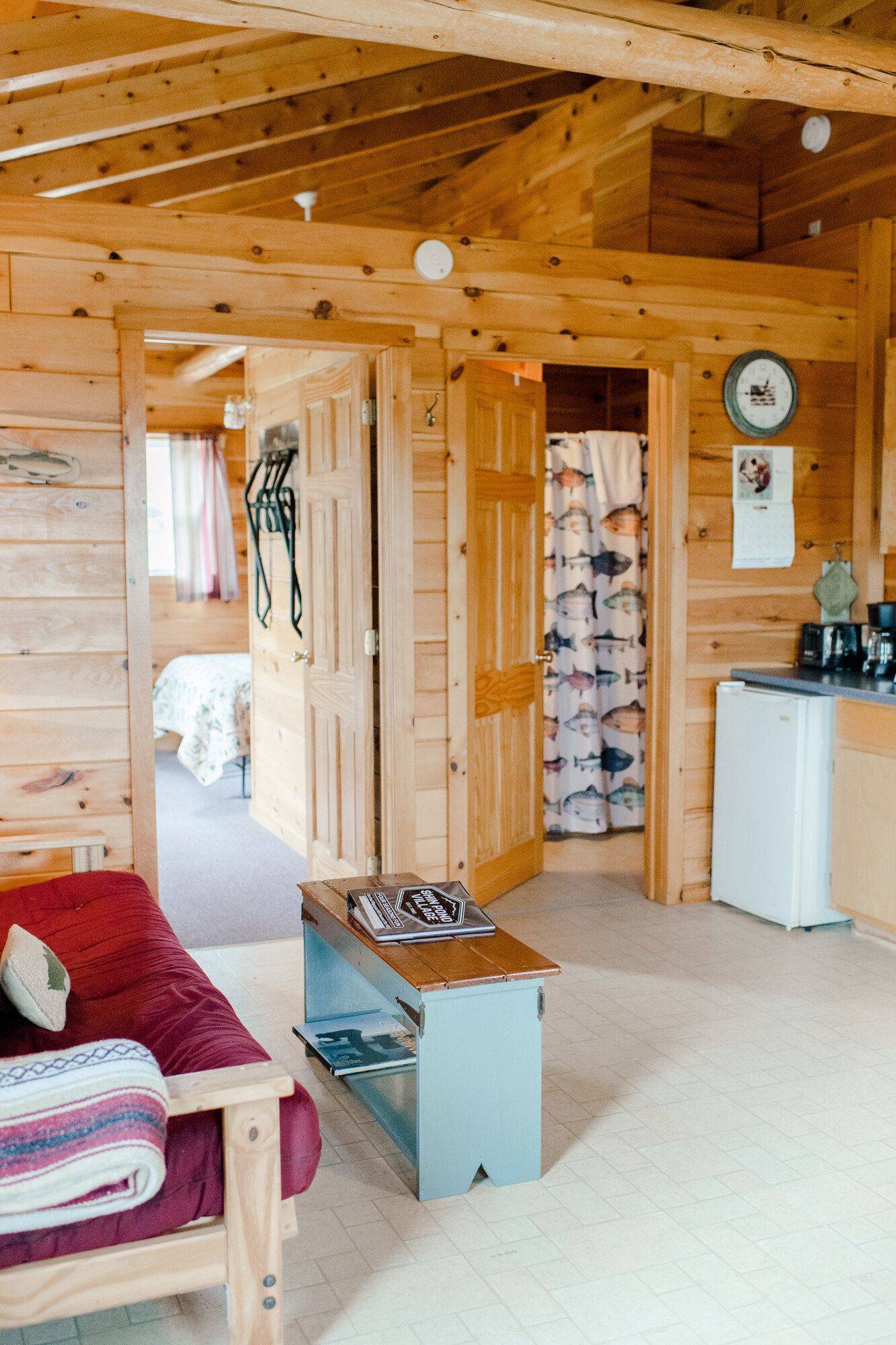 Cozy wood-paneled cabin interior with a red sofa, doorway to bedroom, and small kitchen area