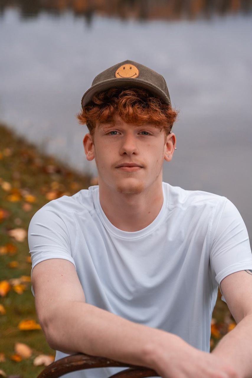 Young person in a white T-shirt and cap sitting outdoors against a blurred autumn background