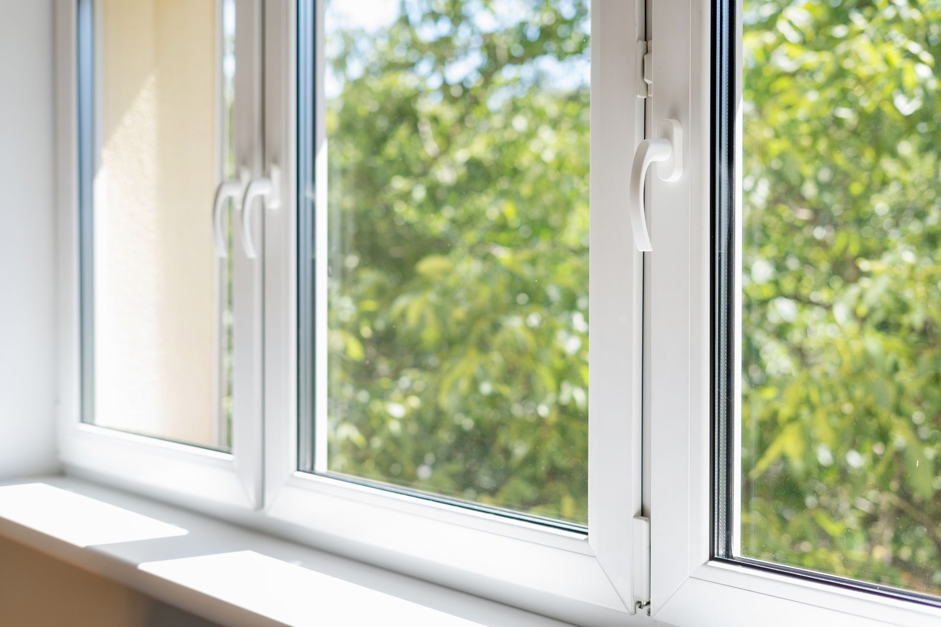 White window with handle, view of green trees and sunny.
