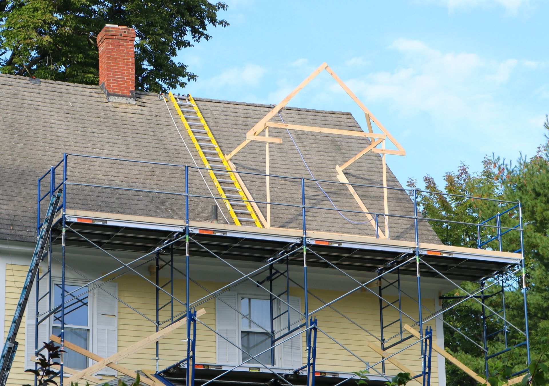 House roof under renovation with scaffolding, ladder, and new roof framing.