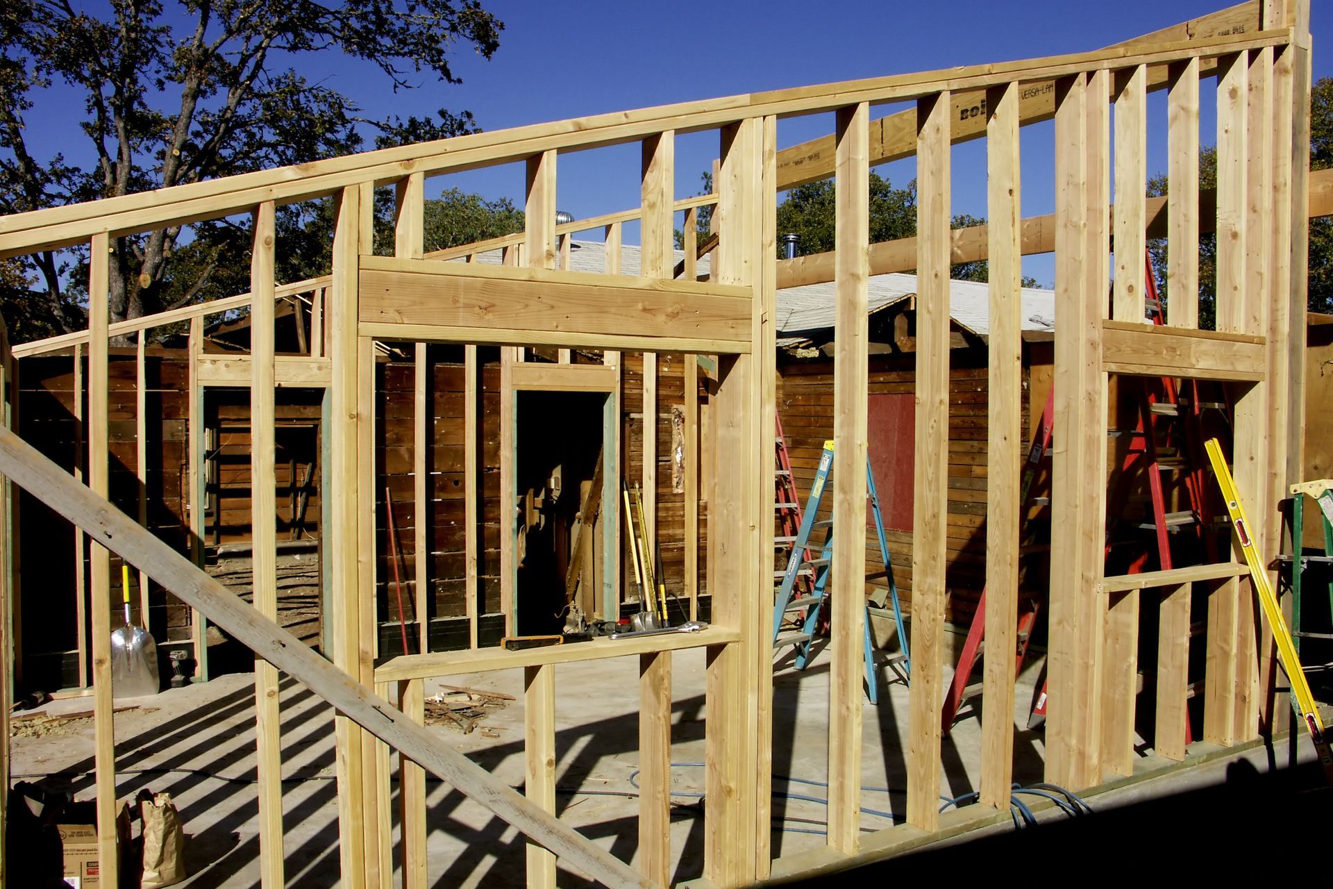 Wood-framed home addition under construction with ladders.