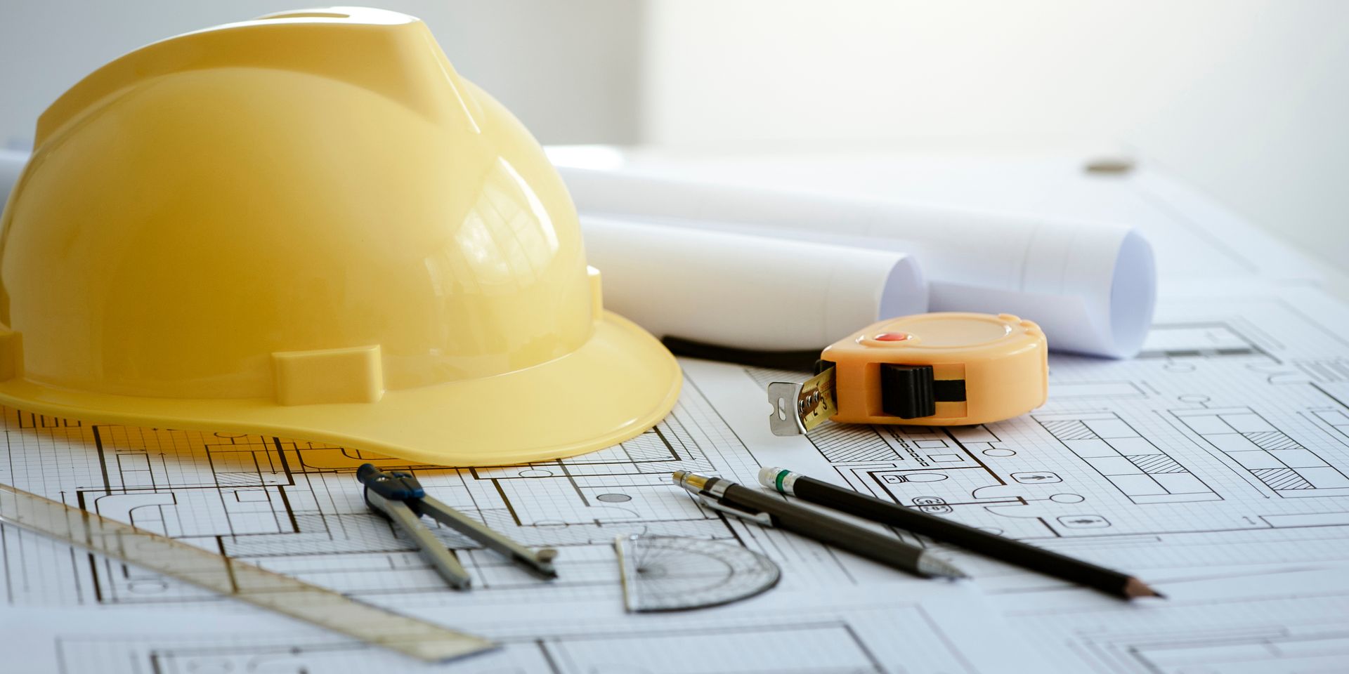 Rolled blueprints, yellow hard hat, and measuring tools on architectural plans