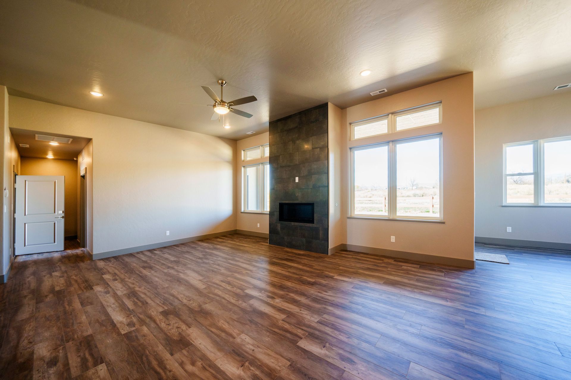 Spacious living room with wood flooring, a fireplace, large windows, and a ceiling fan.