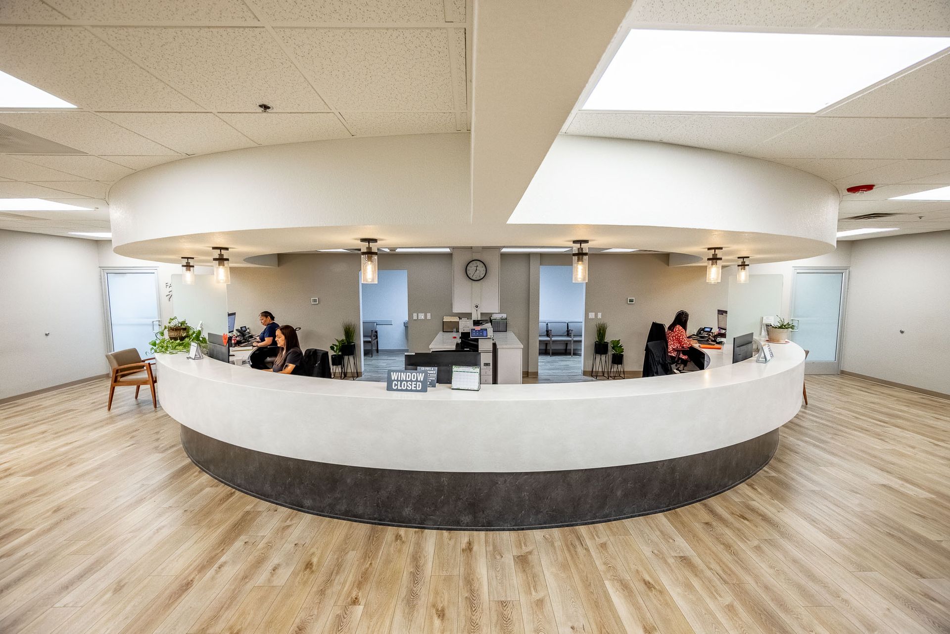 Curved white reception desk in a bright modern lobby with people seated behind it.