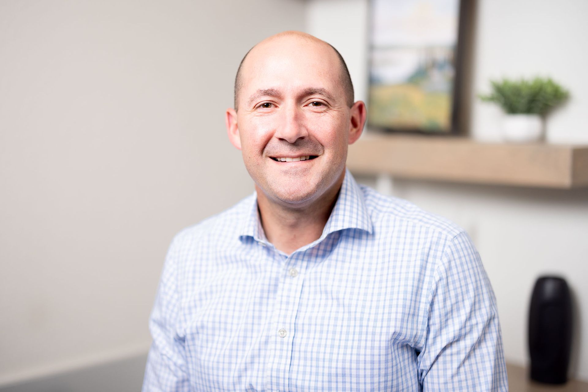 Joseph Hakes, MD in a light blue checkered shirt in a bright office setting