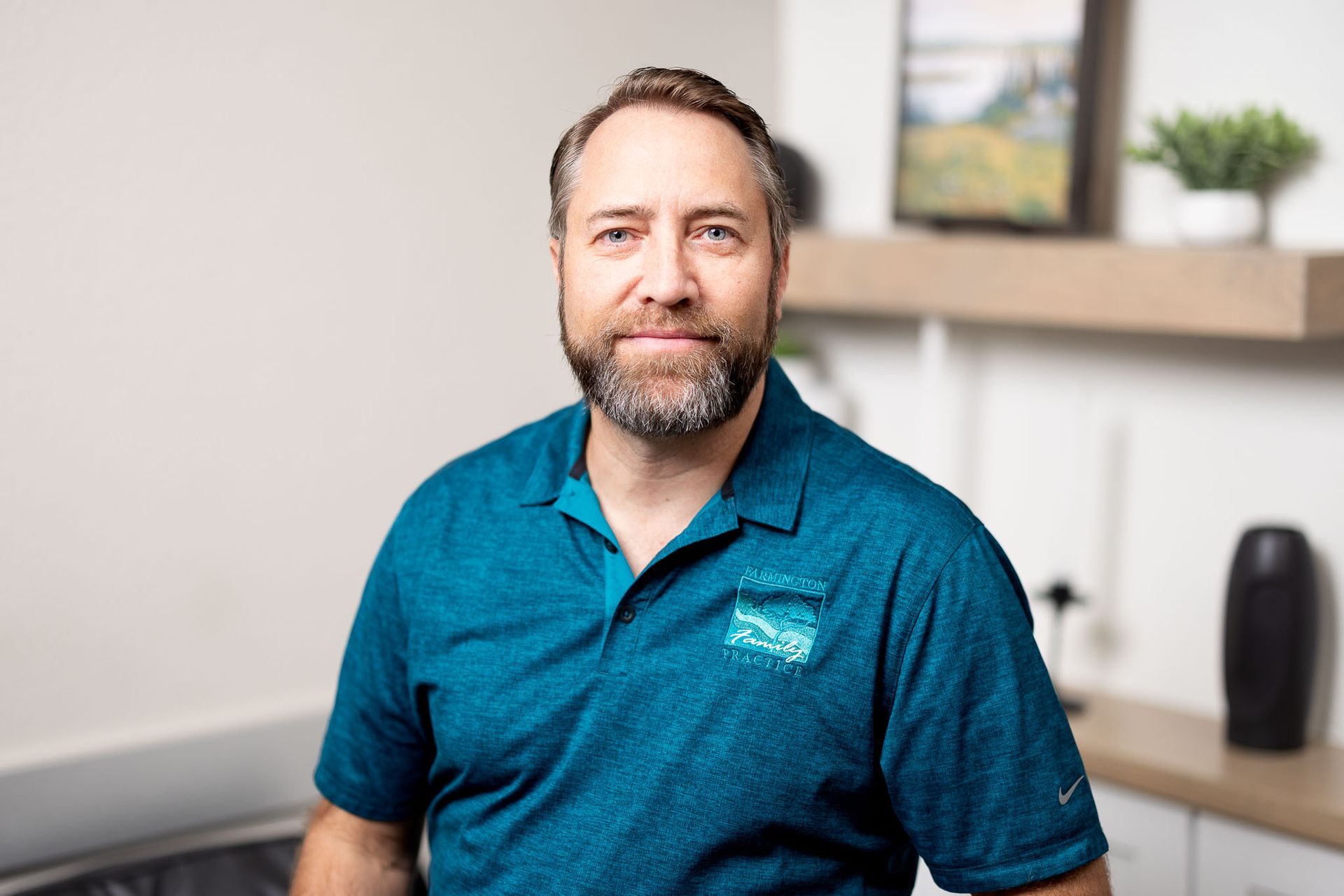 Jonathan Kelly in a teal polo shirt smiling in a bright office setting