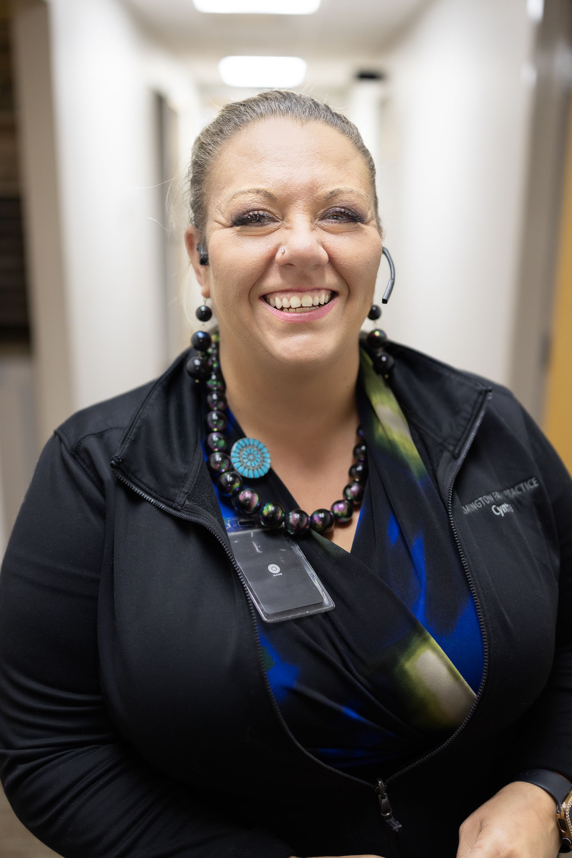 Smiling Farmington Family Practice in a black jacket and blue patterned top standing in a hallway