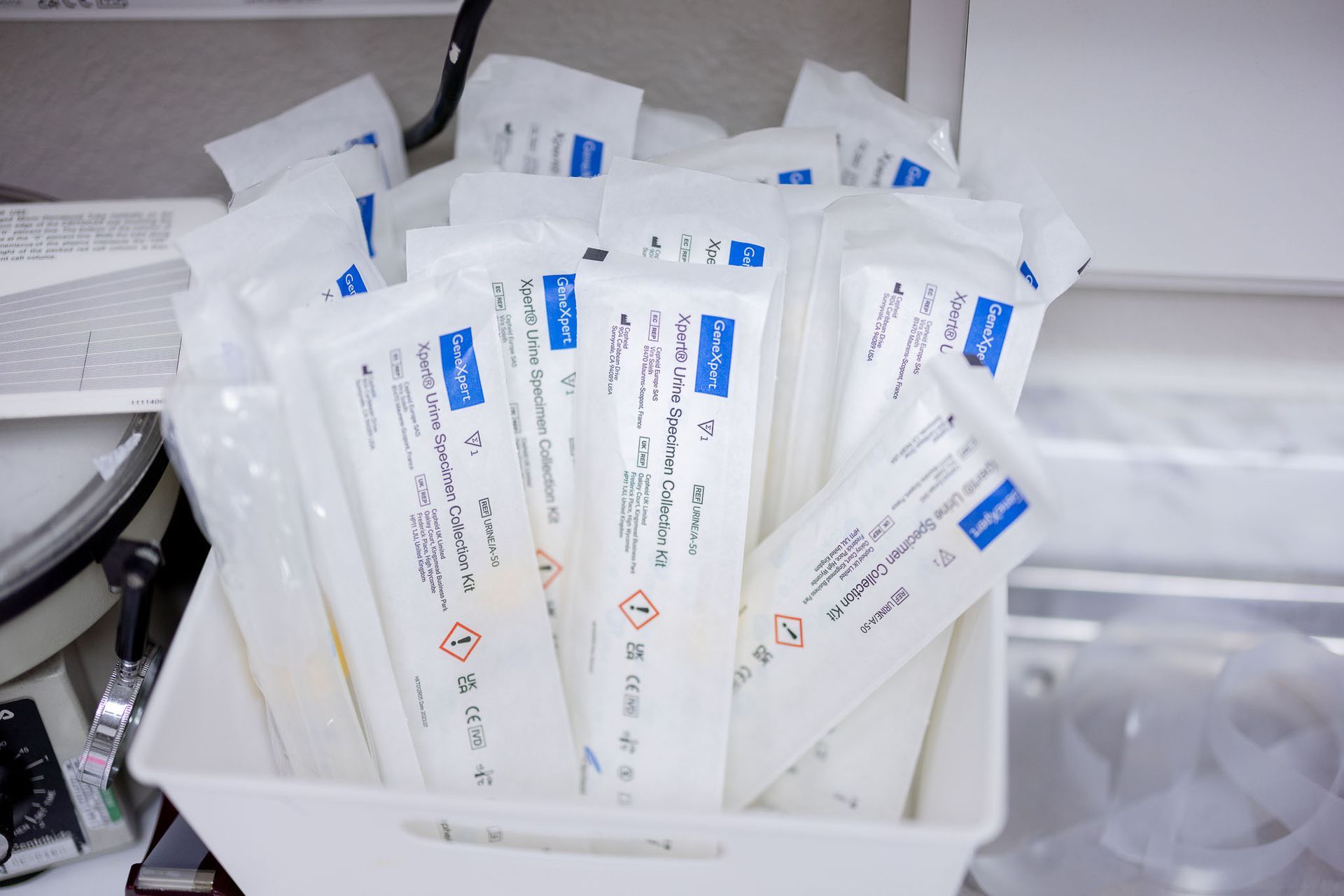 Tray of individually wrapped white test kits with blue labels, stacked in a white bin