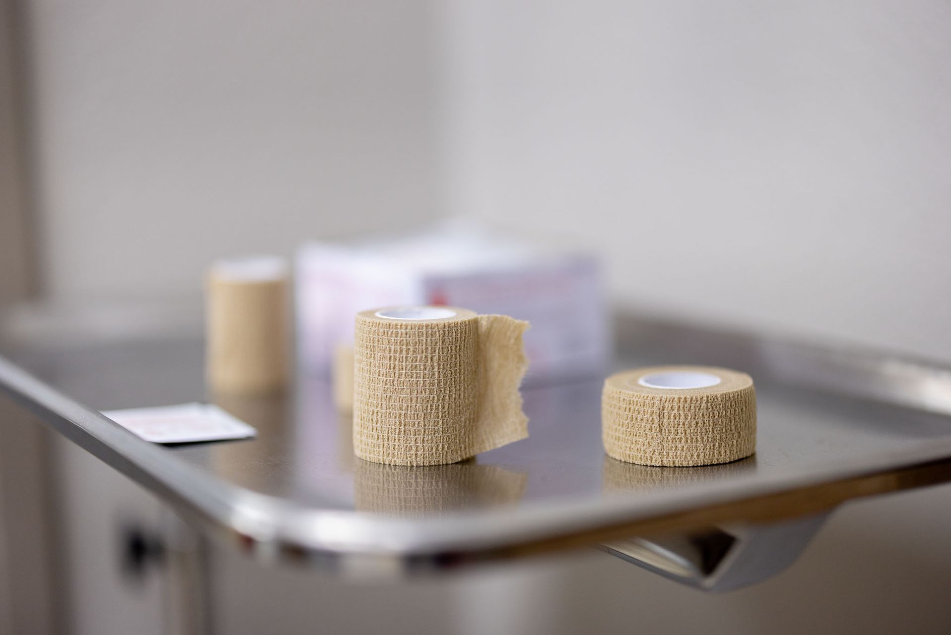 Two beige textured bandage rolls on a metal tray with a blurred clinic background
