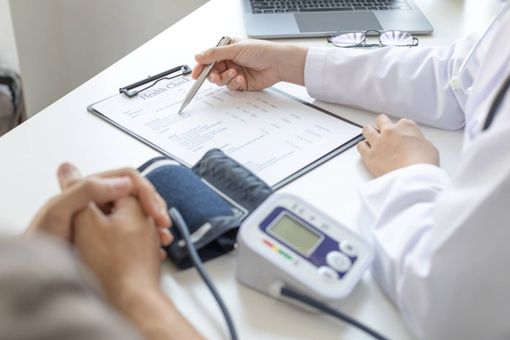 Doctor reviewing medical chart with patient’s blood pressure being measured on a desk
