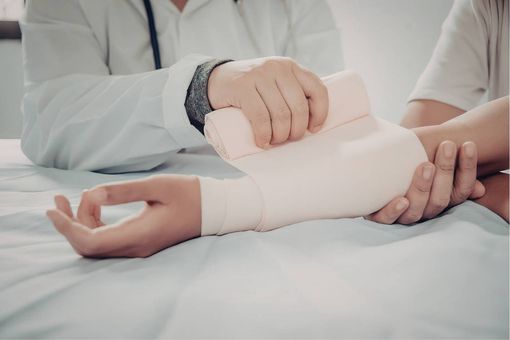 Nurse wrapping a patient's wrist with a white bandage on a hospital bed