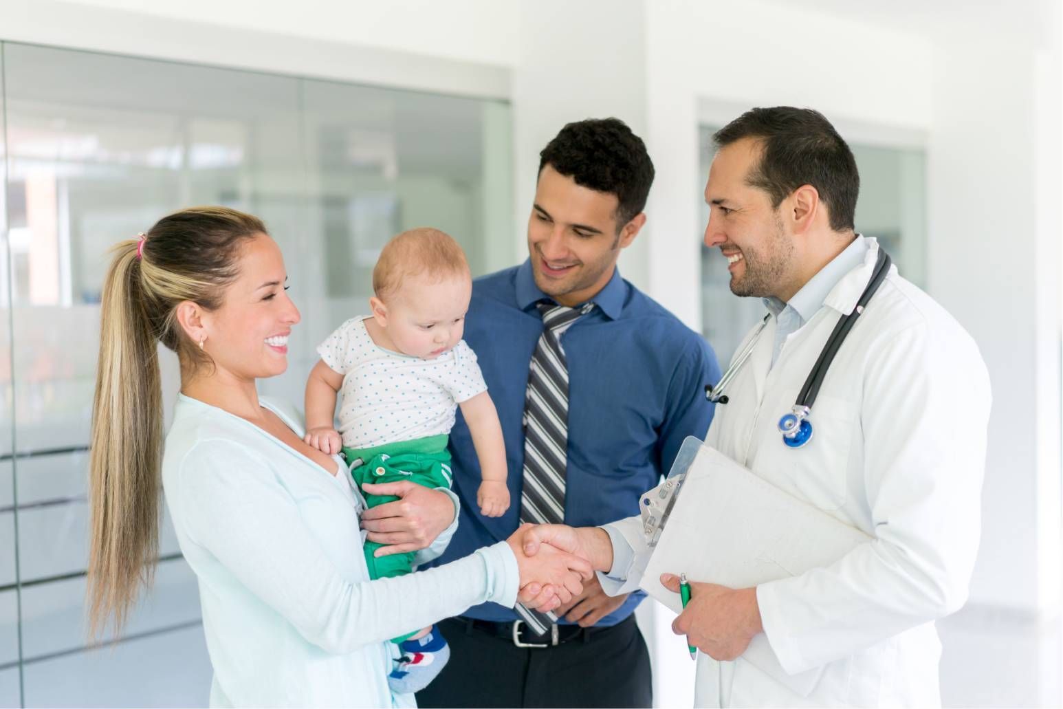Doctor shaking hands with a parent holding a baby in a bright clinic hallway