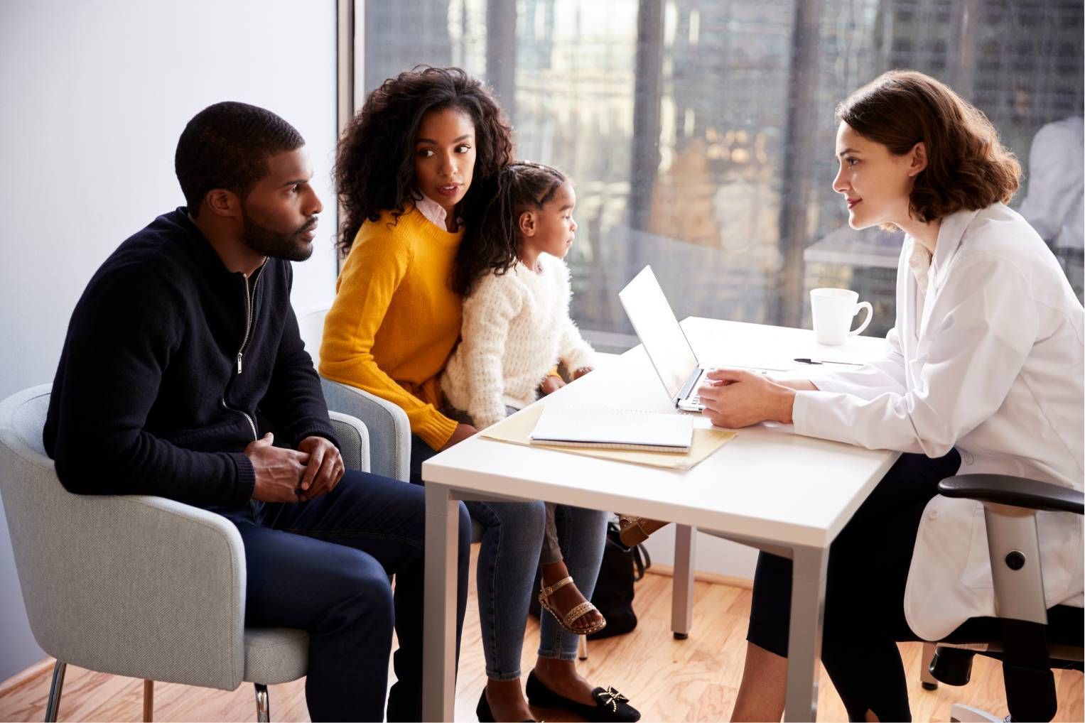 Counselor meeting with a family at a table, discussing paperwork on a laptop in a bright office.
