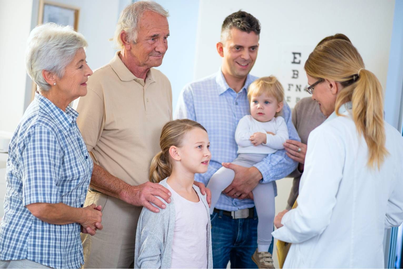 Family in a clinic with a doctor examining a baby and smiling parents and grandparents nearby
