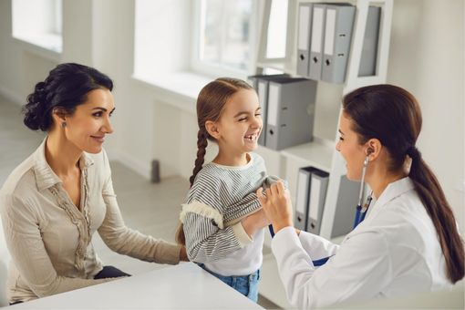 Doctor examining a smiling child while her parent sits nearby in a bright clinic office