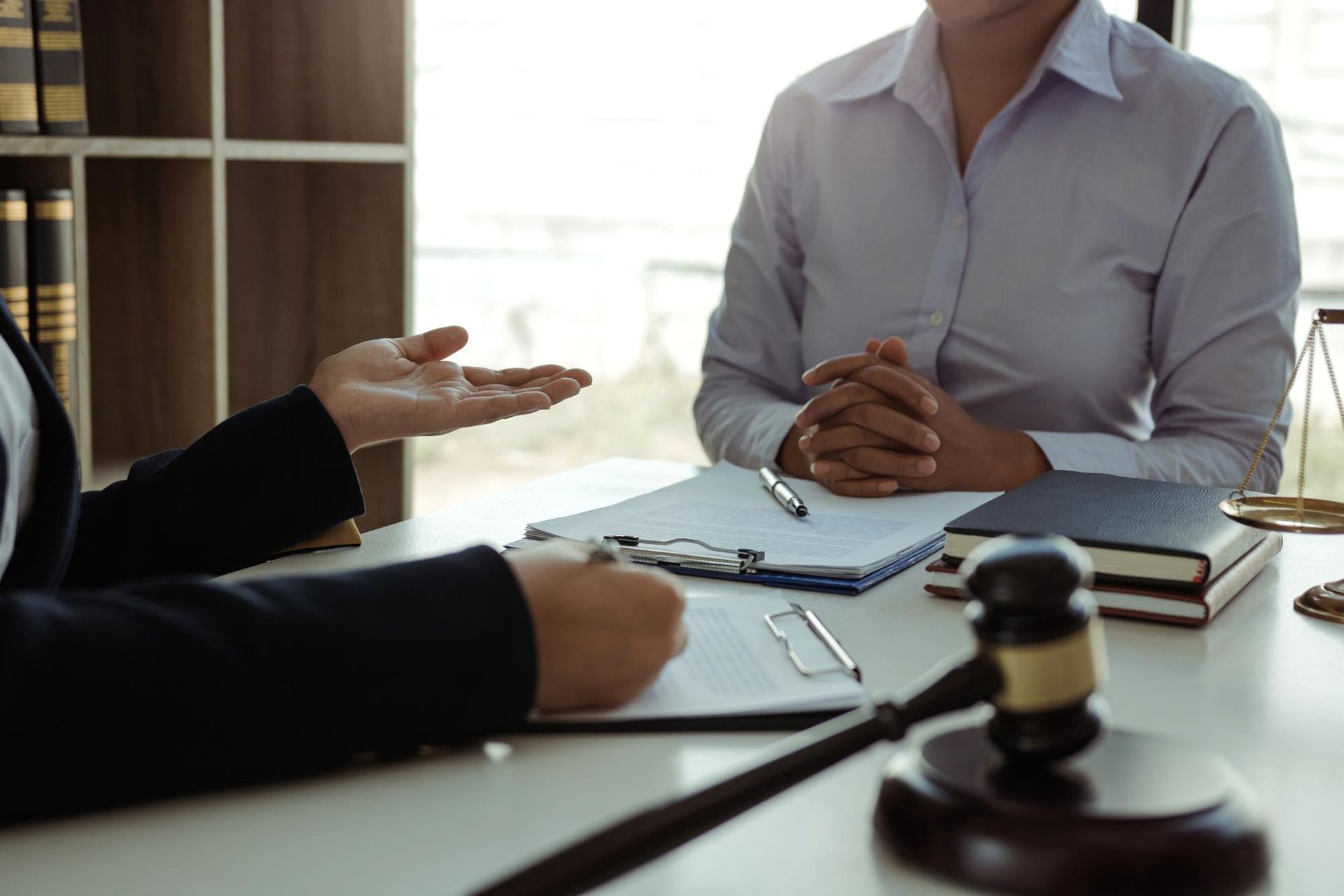 Lawyer in suit gestures while consulting with client. Gavel and documents on table.