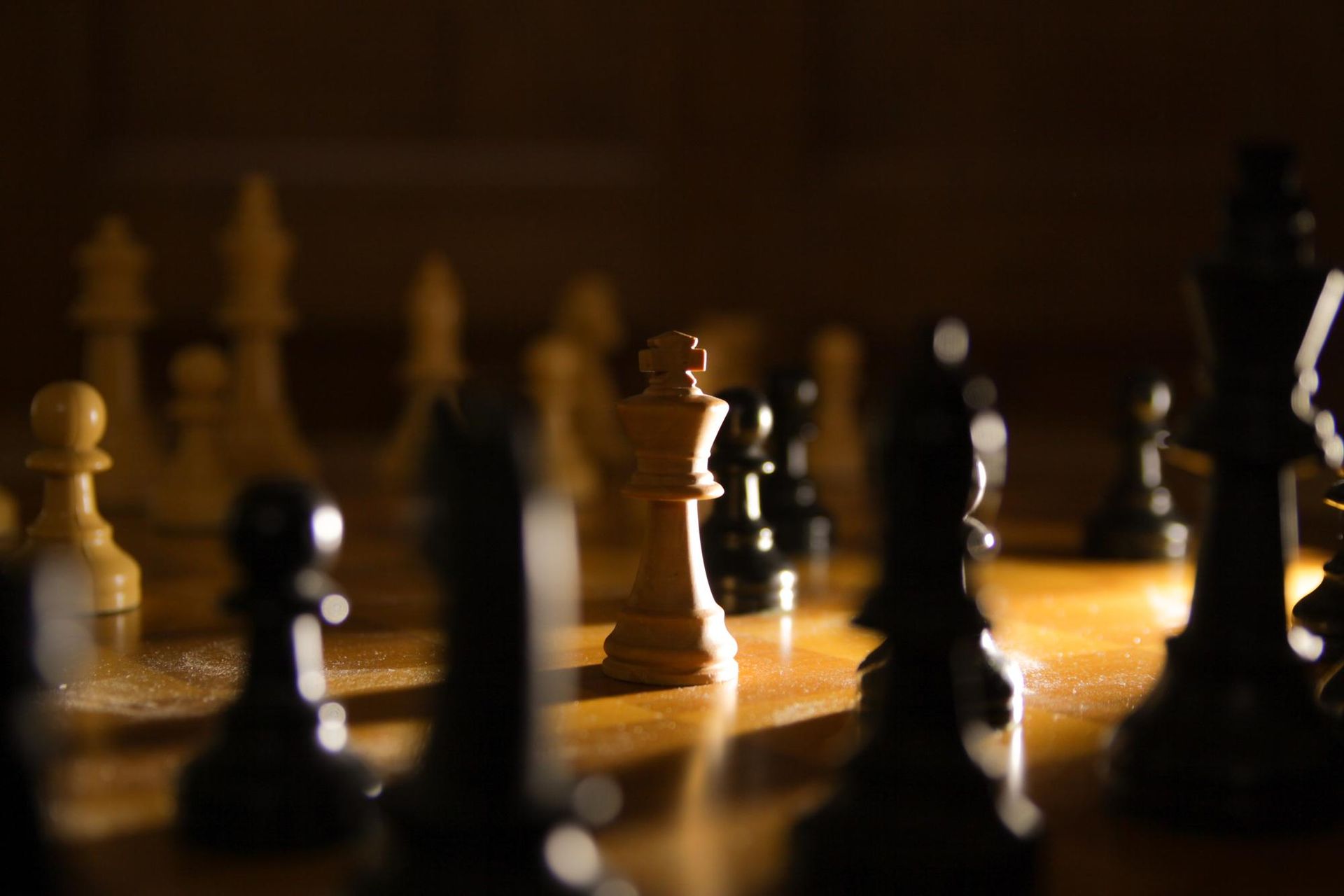 Chessboard with black and white pieces; white king is center focus, backlit in shadow.