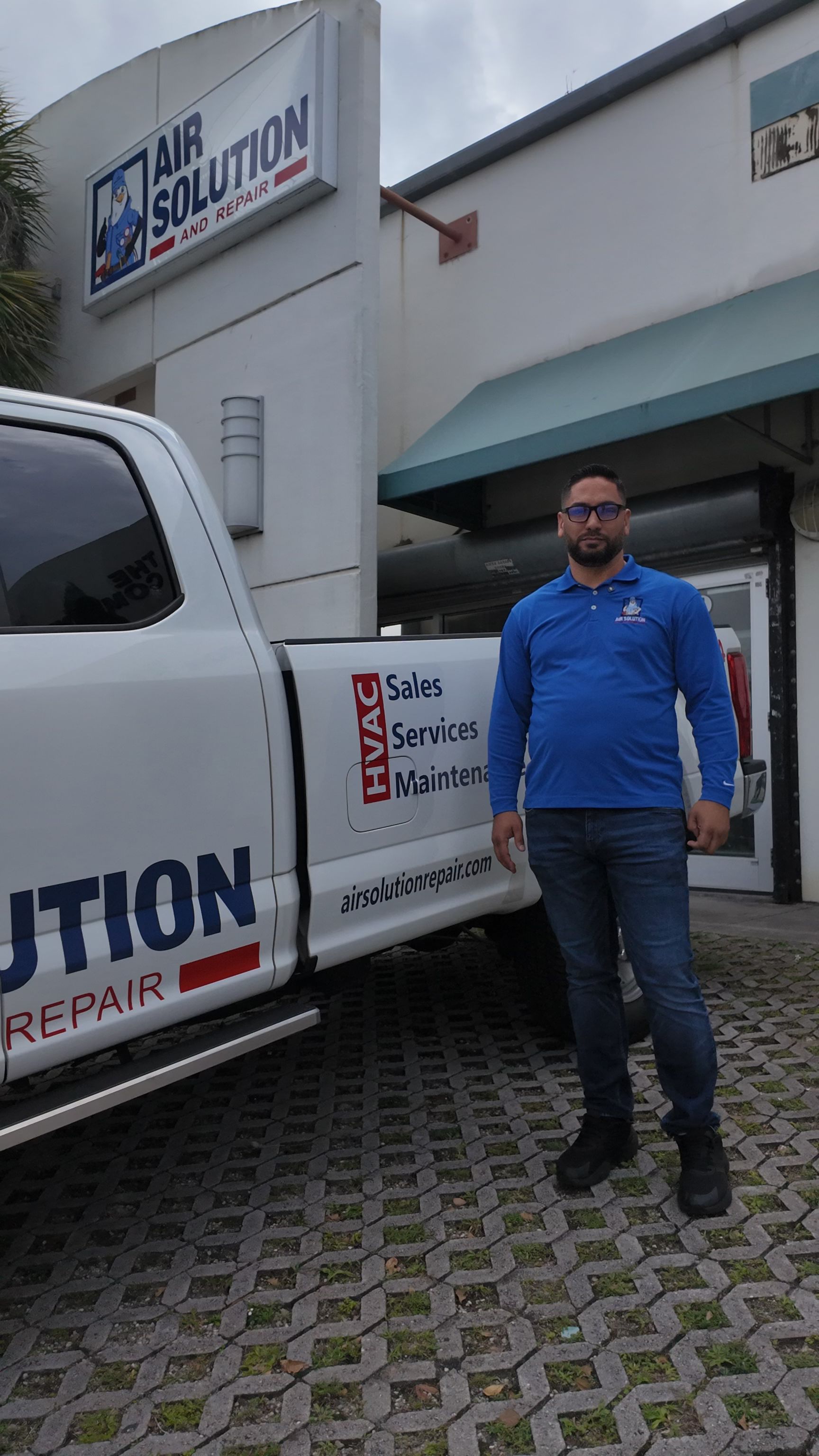 Man standing beside a white service van outside a building with a blue awning