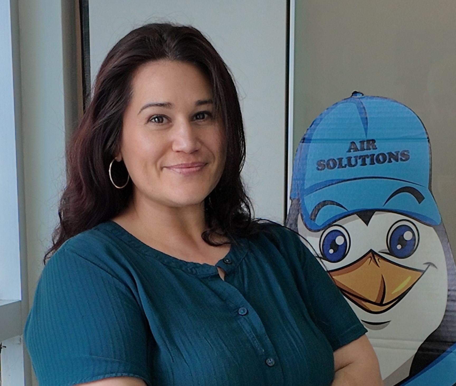 Woman smiling beside an Air Solutions mascot sign in an office setting