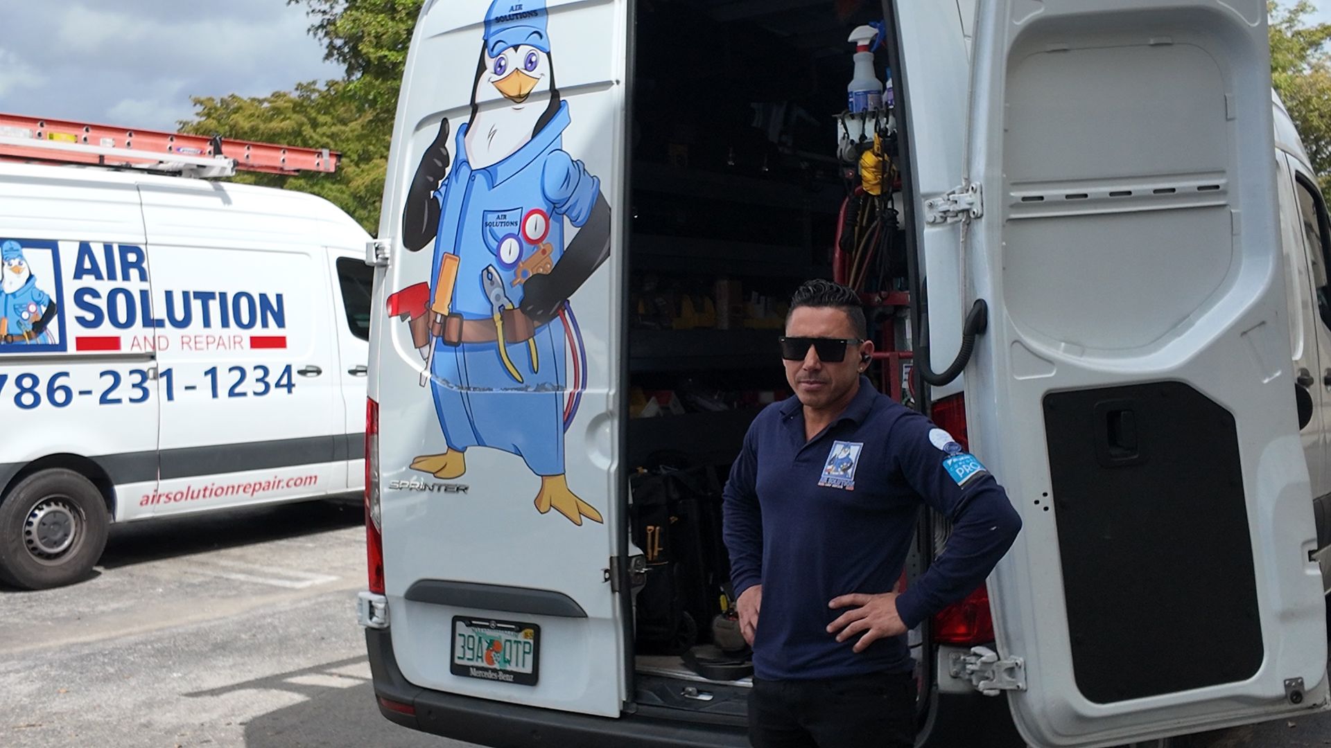 Man standing by open van doors beside a blue cartoon graphic, with an AIP Solution truck in the background