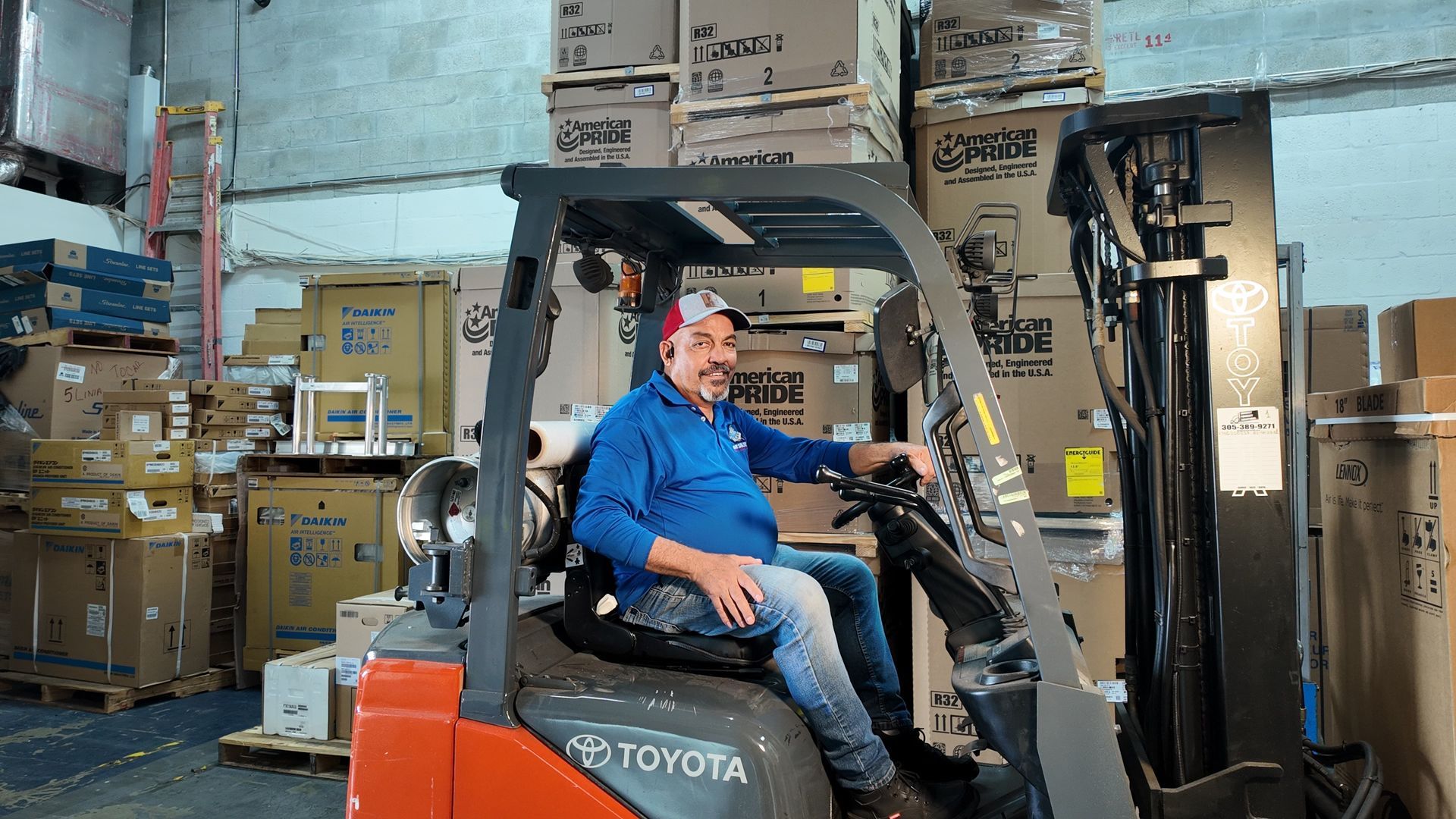 Worker in blue shirt sitting on an orange Toyota forklift in a warehouse aisle