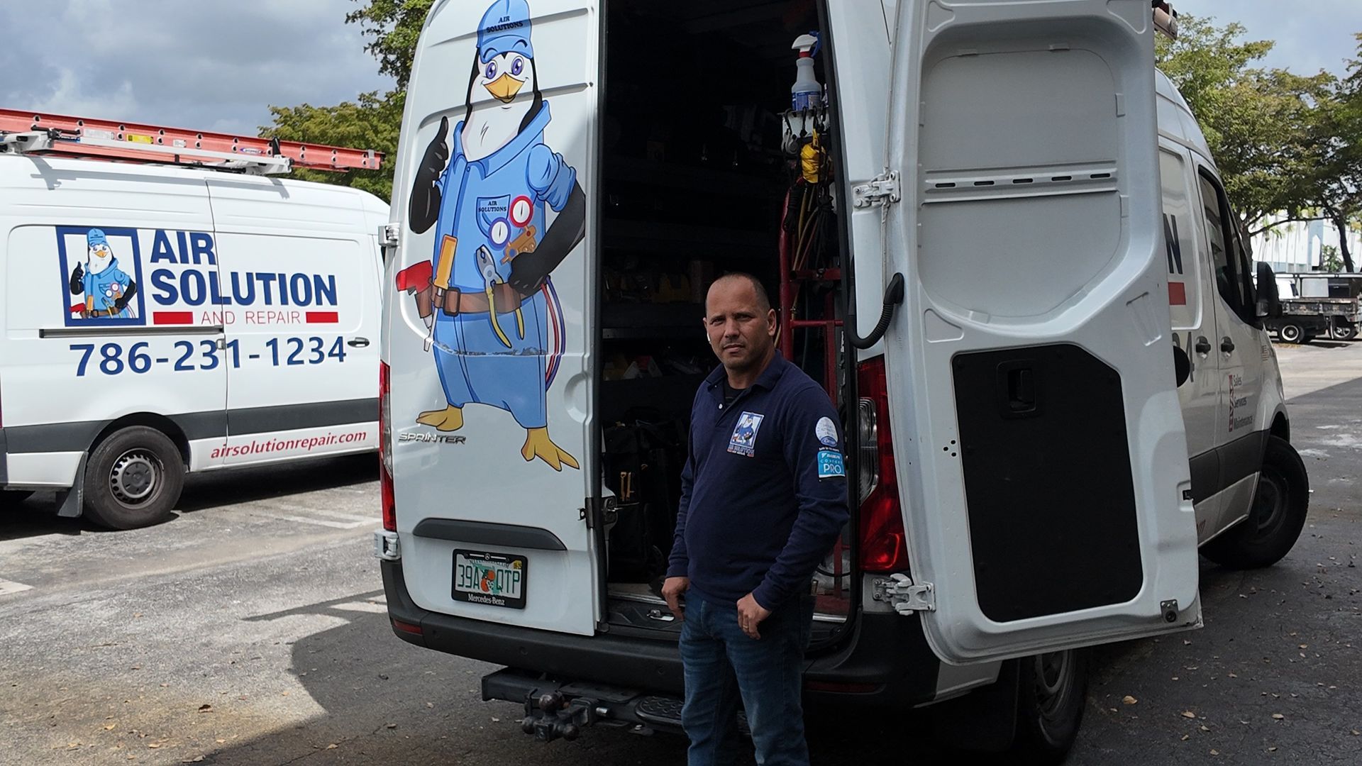 White service van with open rear door; technician stands beside it in a parking lot, with Air Solutions van in background