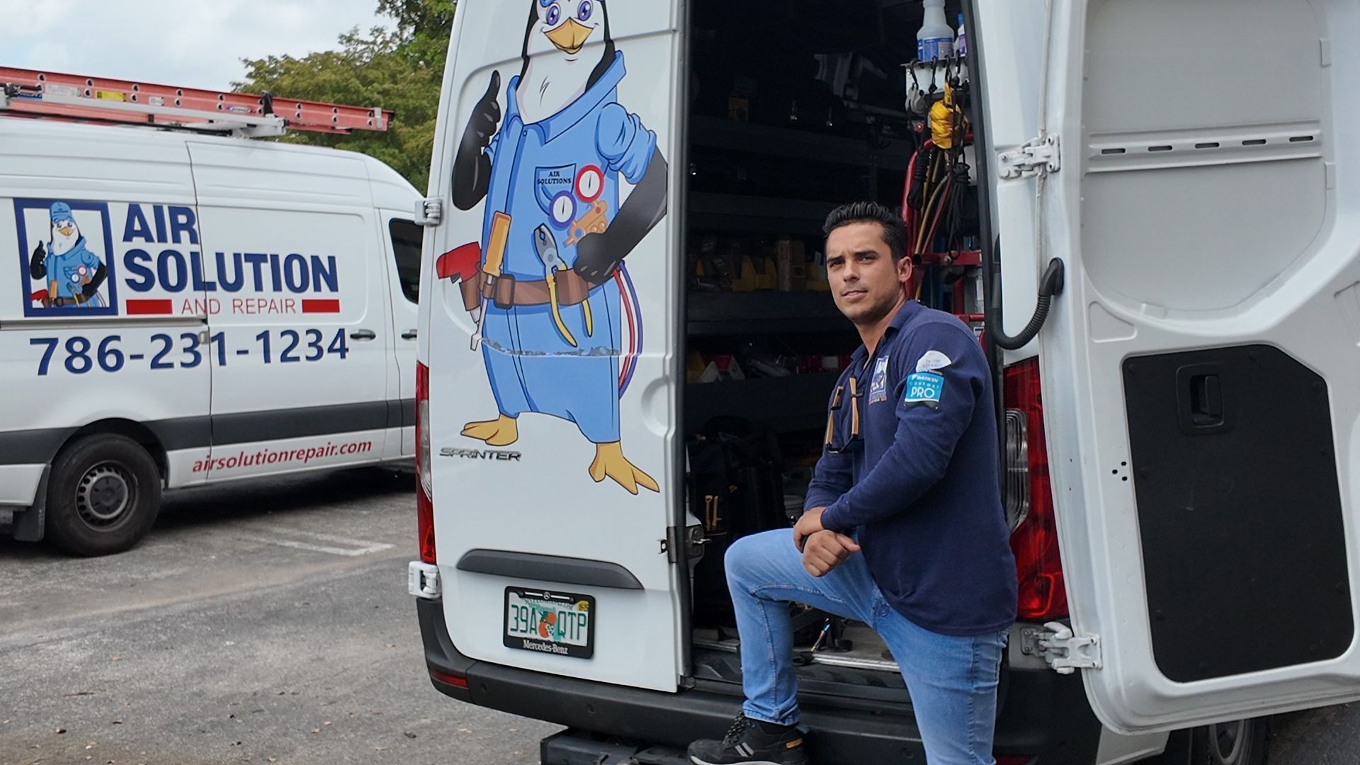 Man sitting on the back of a white Air Solution van beside a cartoon air conditioning graphic.