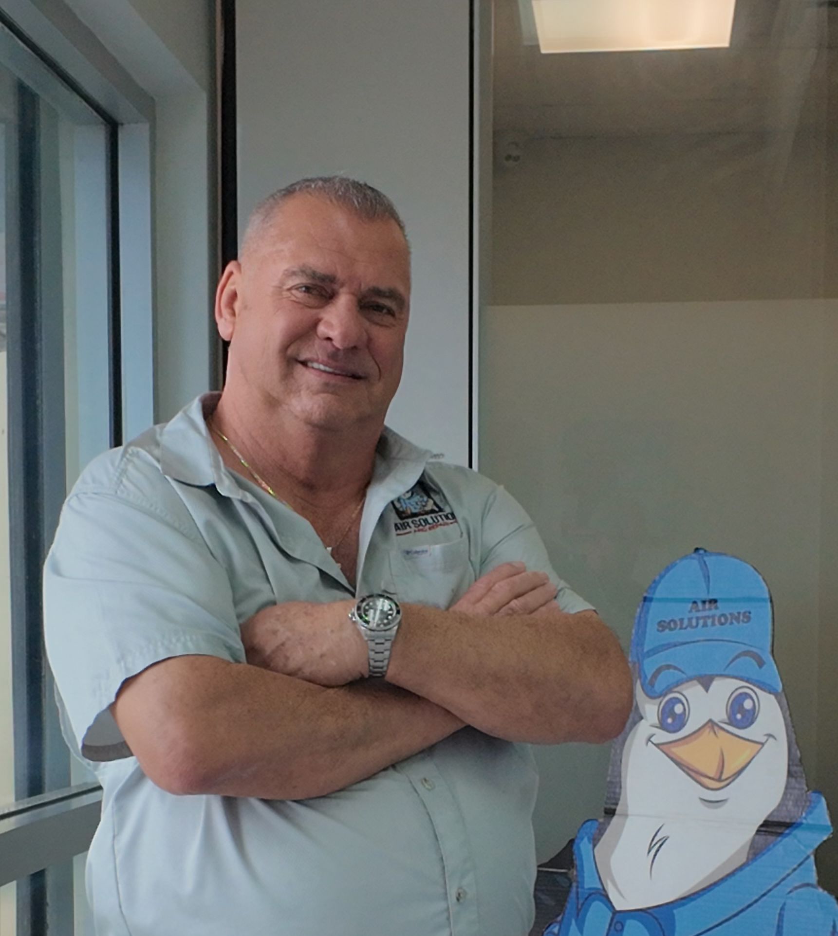 Smiling man with crossed arms beside a blue bird cutout in an office setting