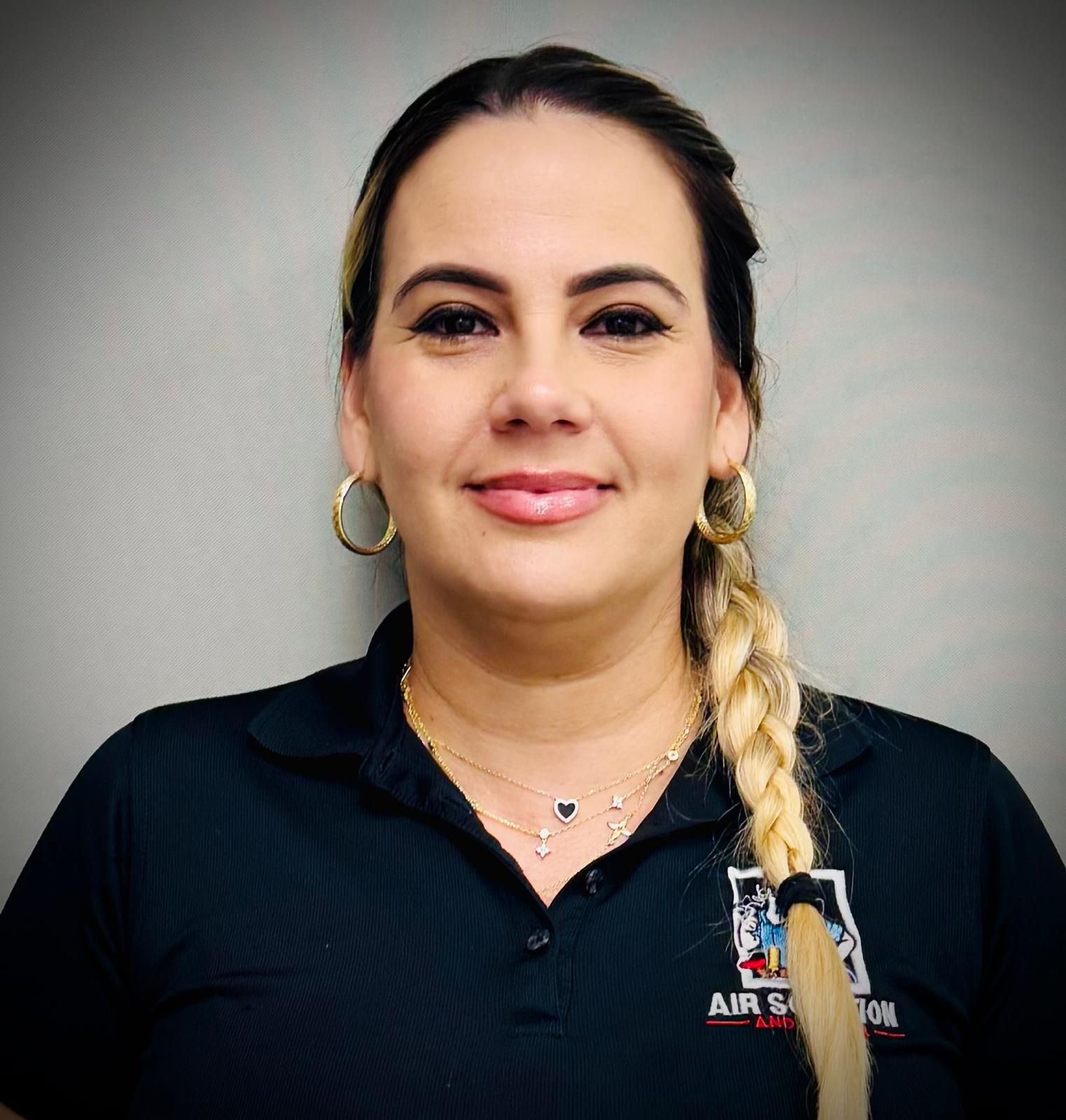 Portrait of a woman in a black shirt with a blonde braid, standing against a gray background.