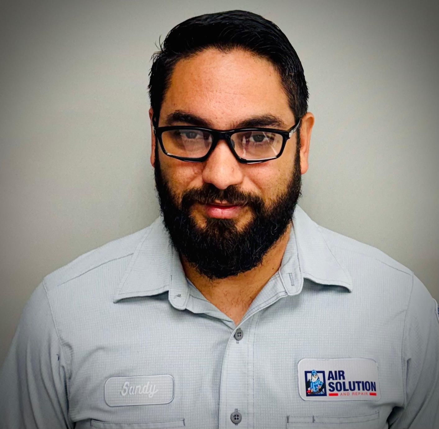 Man with glasses and beard wearing a light gray collared shirt against a plain background