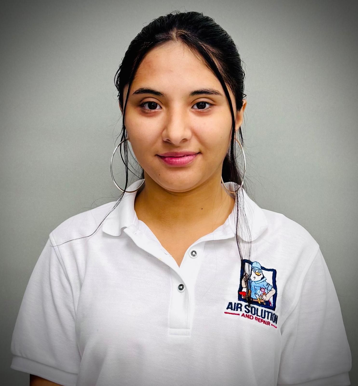Portrait of a woman in a white polo shirt with a logo, standing against a gray background