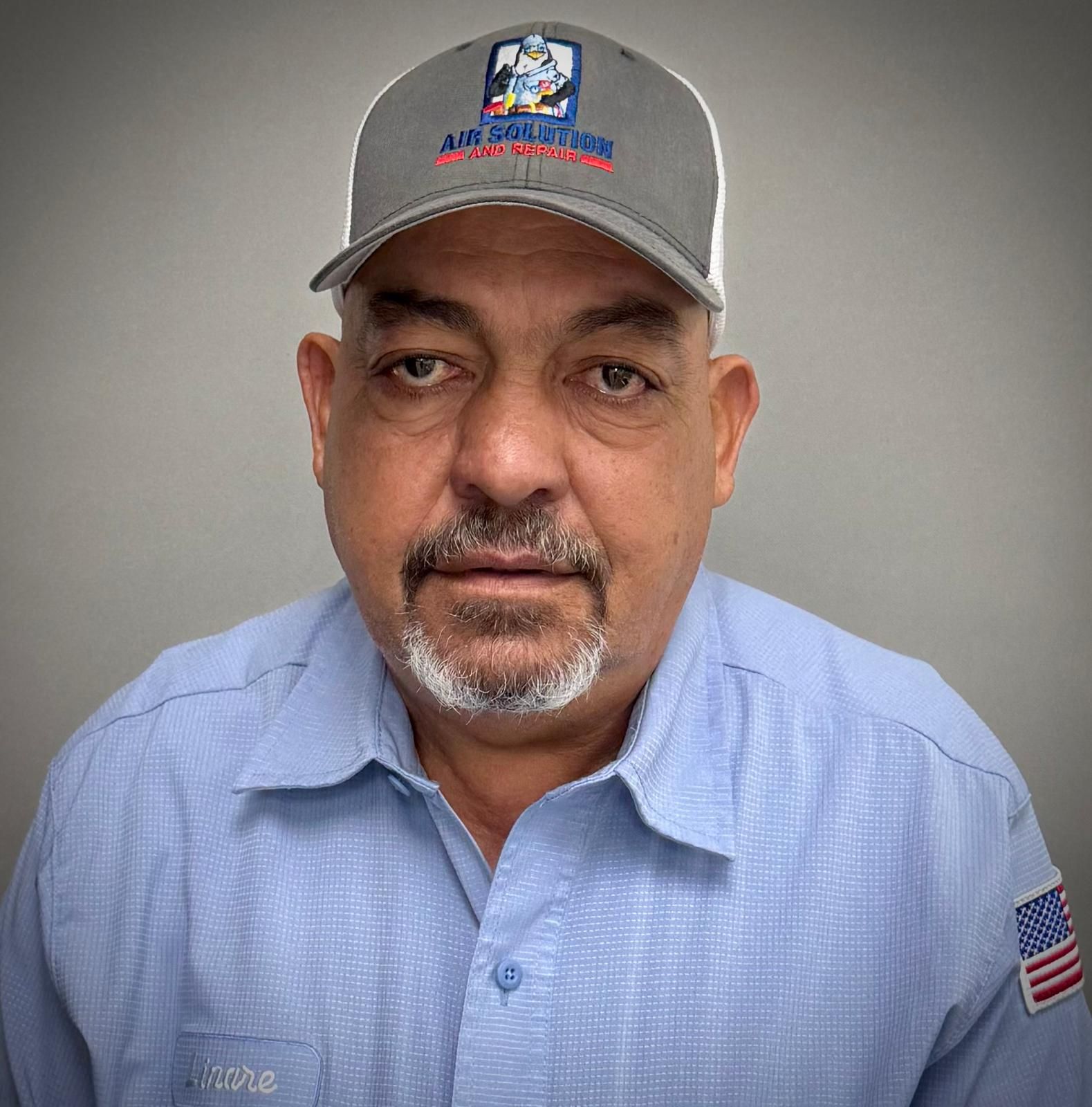 Man in gray cap and light blue shirt against a gray background, facing the camera.