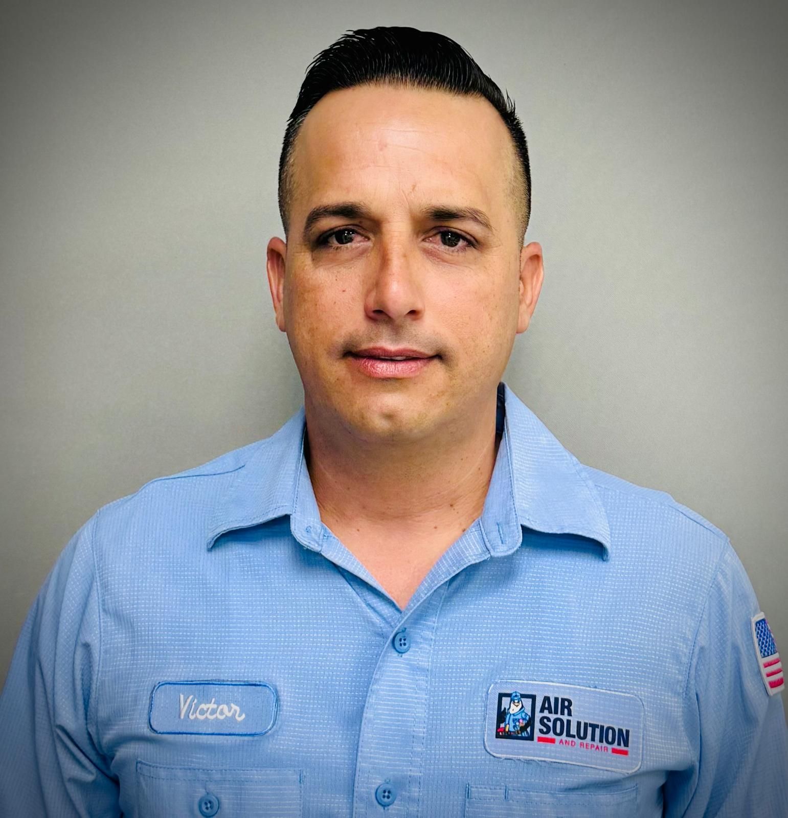 Portrait of a man in a light blue collared shirt with an Air Solution logo, standing against a gray background