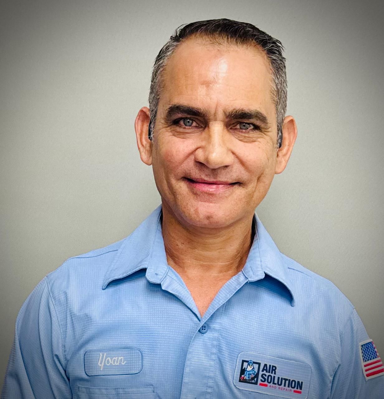 Portrait of a man in a light blue work shirt with an Air Solutions logo, smiling against a gray background