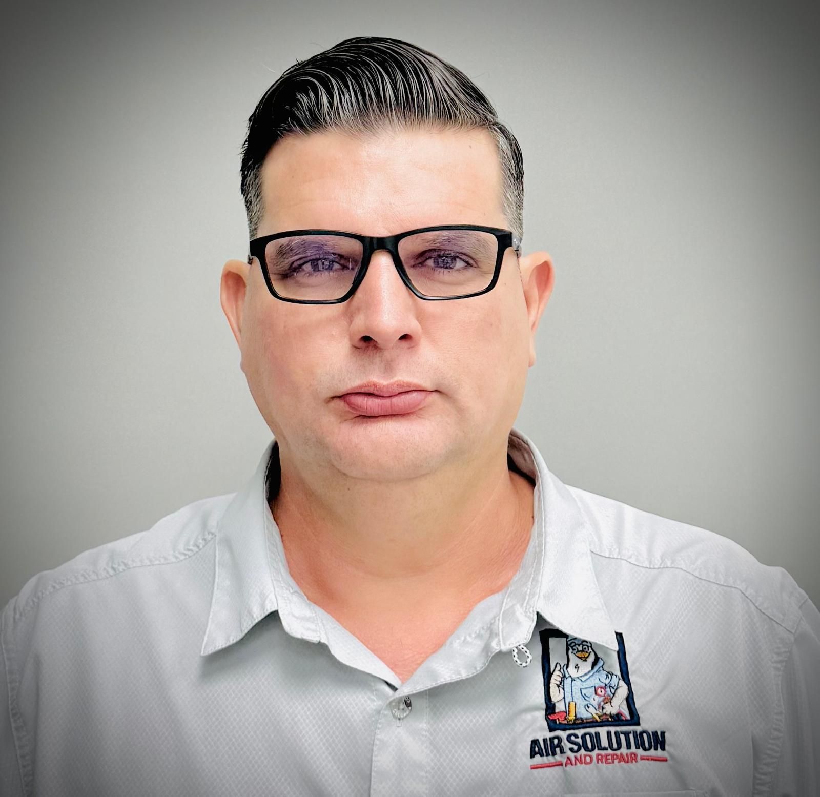 Man in glasses wearing a white shirt with an Air Solution logo, against a gray background.