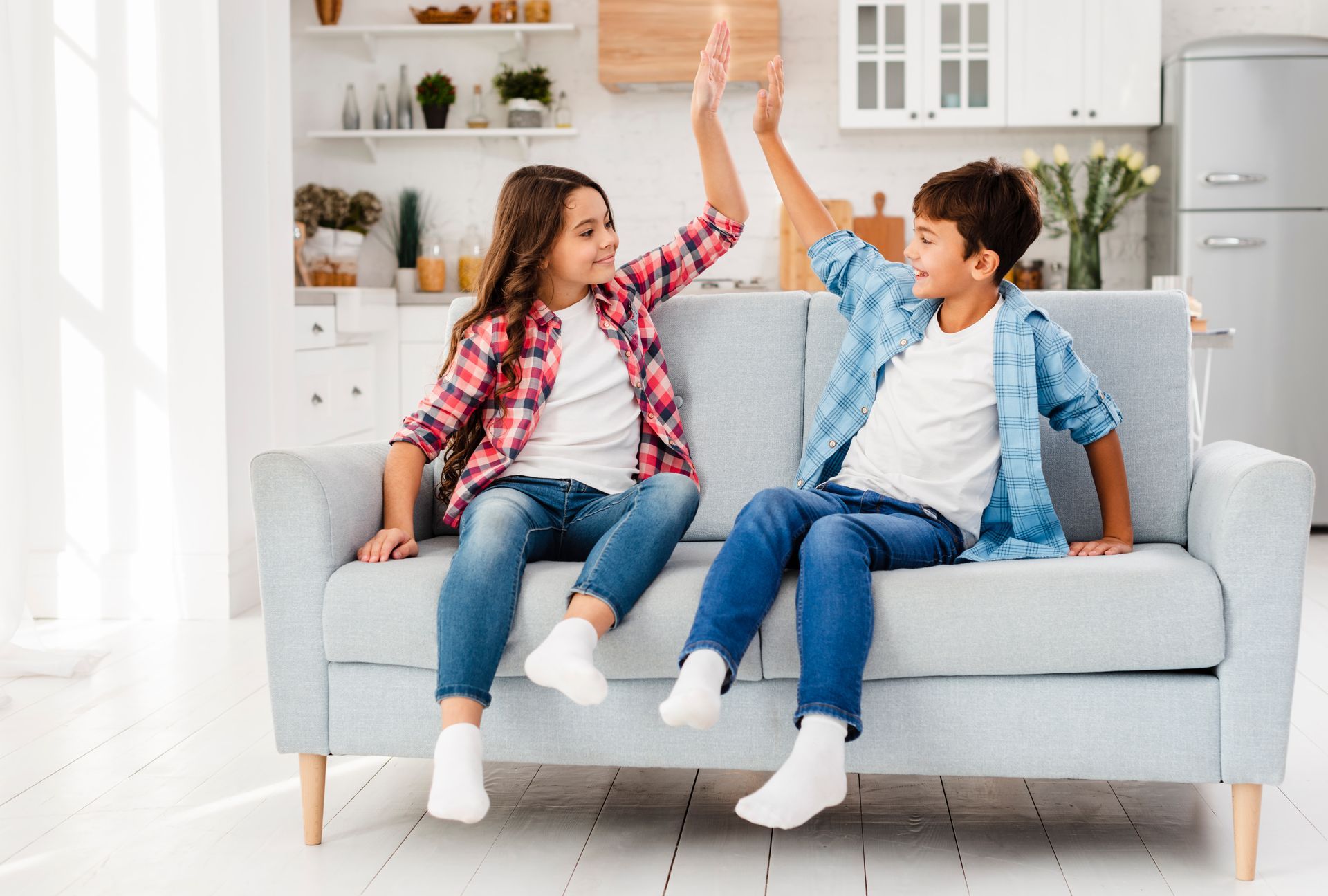 Two children high-five on a light blue couch in a bright living room