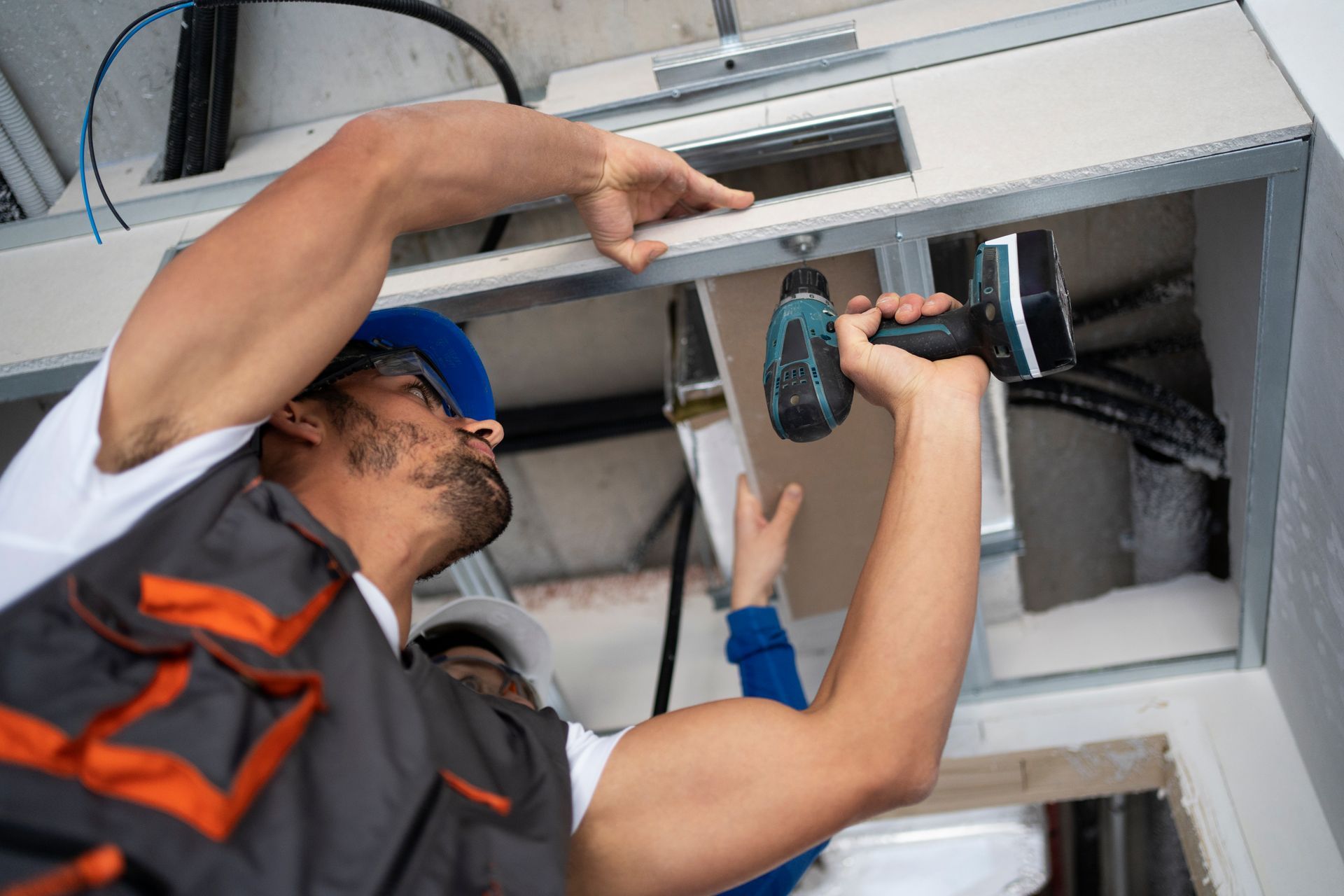 Two technicians installing a ceiling light fixture with a power drill in an indoor workspace