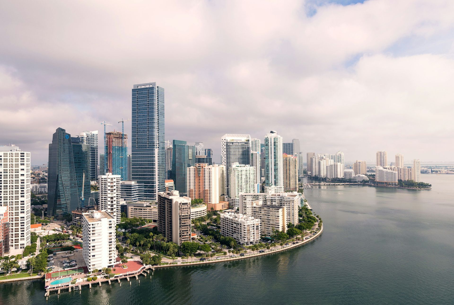 City waterfront skyline with tall modern buildings beside a curved bay under a cloudy sky