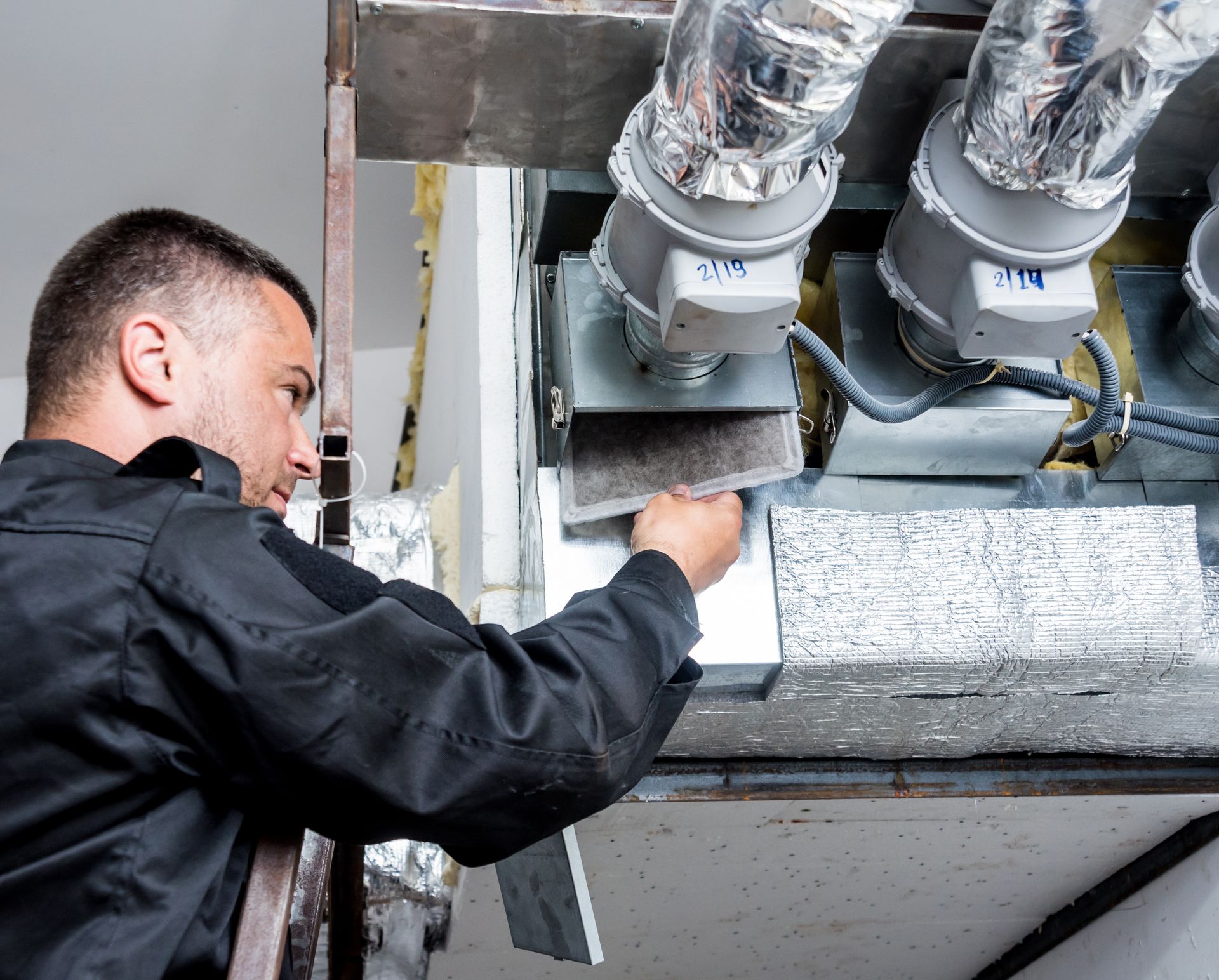 Worker inspecting industrial ducts with a tool in a mechanical equipment room