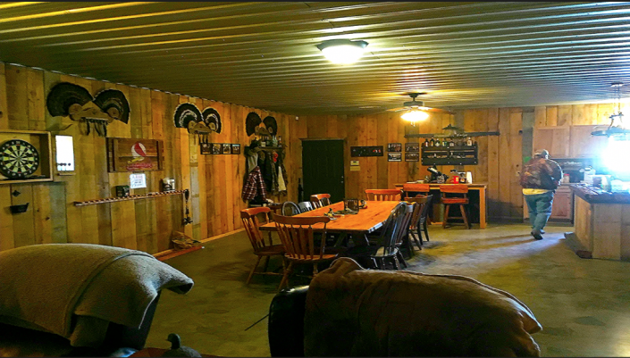 Rustic lodge dining room with wooden tables, warm lighting, dartboard, and mounted antlers.