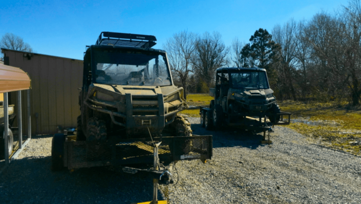 Two off-road utility vehicles parked outside a building on a gravel lot under a clear blue sky