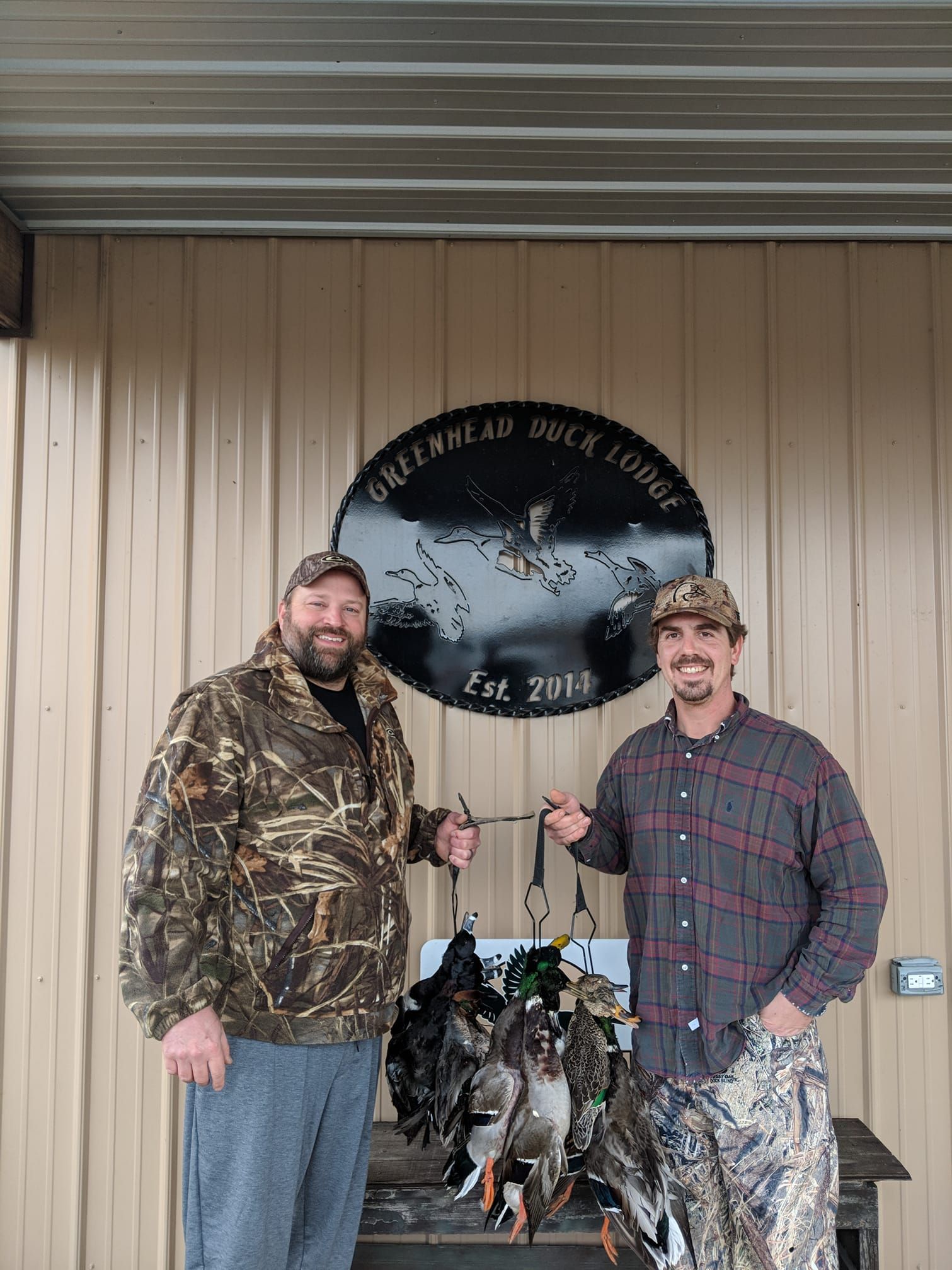 Two hunters pose with a hanging flock of birds under a hunting club sign.